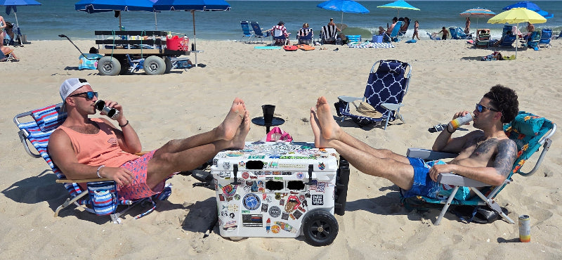 Two Broskiez sitting on beach chairs with a cooler box between them, enjoying drinks on a sunny day.